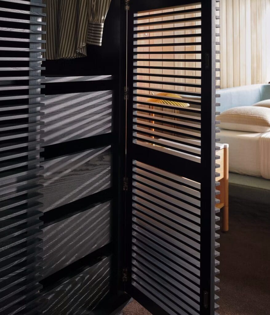 A close-up view of a stylish room divider with horizontal slats, showcasing shadow patterns on the floor and a glimpse of a modern living room in the background.