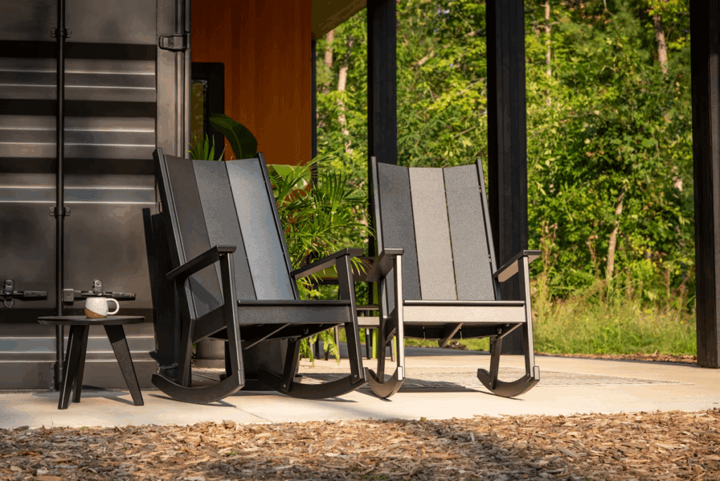 Two modern rocking chairs positioned on a patio, with a small side table holding a coffee cup, and lush greenery in the background.
