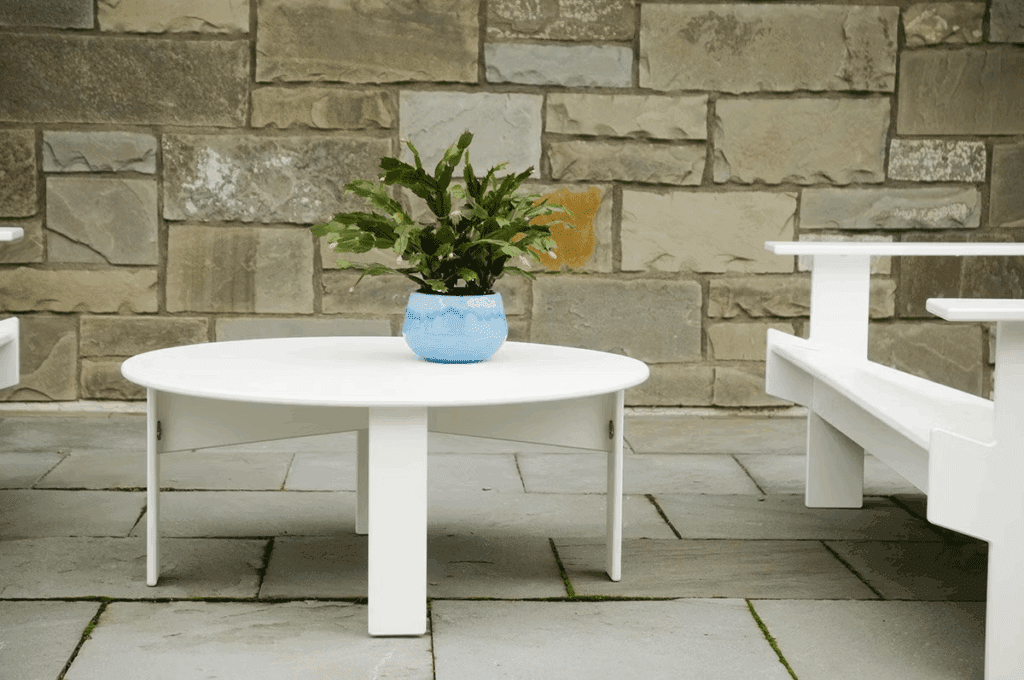 Modern outdoor seating area featuring a round white table with a blue potted plant, set against a textured stone wall.