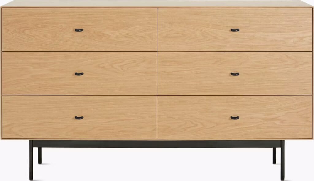 A wooden dresser with six drawers featuring black handles, resting on thin black metal legs.
