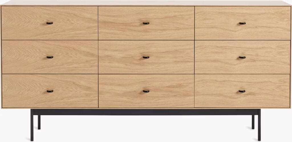A wooden dresser with nine drawers, featuring a light oak finish and black handles, set on slender black legs.