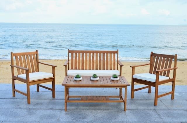 Wooden outdoor seating set with a bench and two chairs, accompanied by a coffee table, overlooking a sandy beach and ocean view.