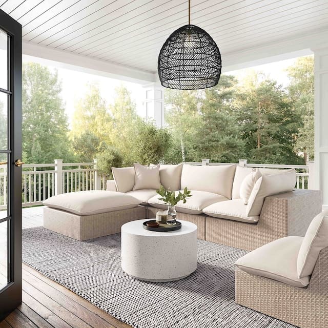 Stylish outdoor living space featuring modern beige sofas, a round table, and a black pendant light, surrounded by greenery.
