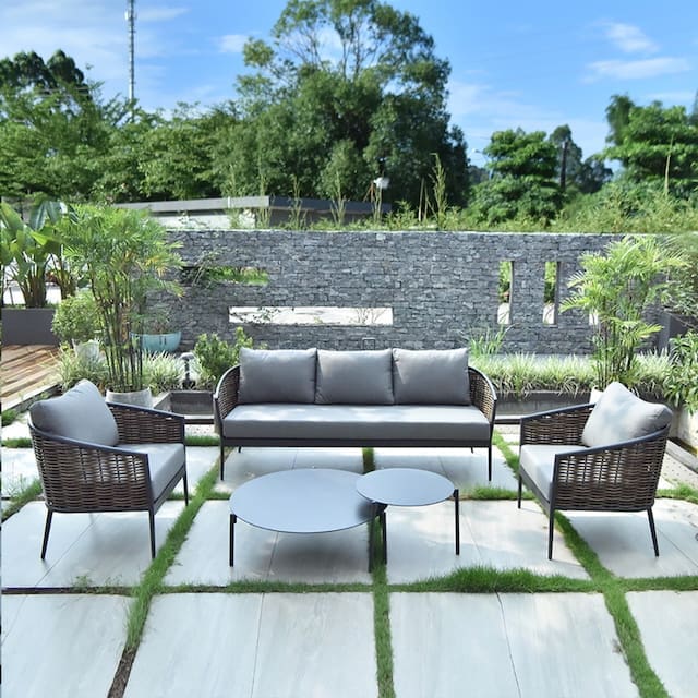 Stylish outdoor seating area featuring a gray upholstered sofa and chairs, surrounded by greenery and a stone wall.