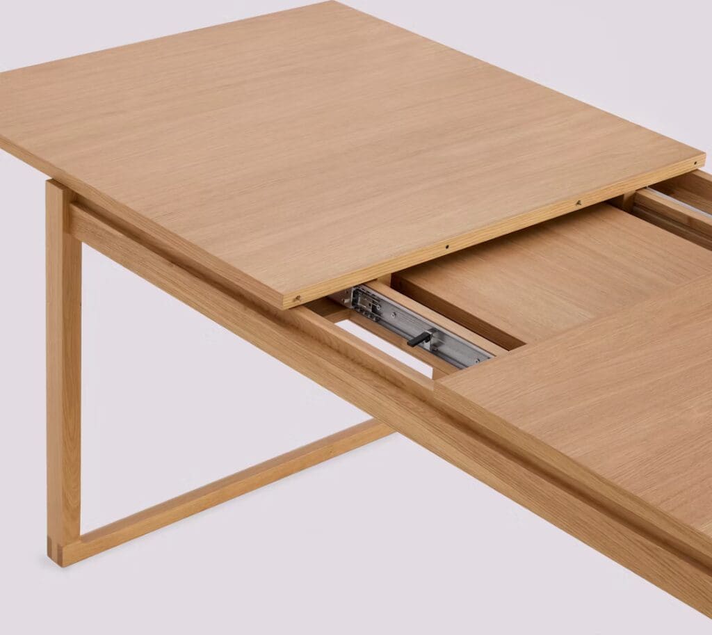 Close-up view of a wooden dining table featuring a smooth finish and a sliding top mechanism for extending its length.