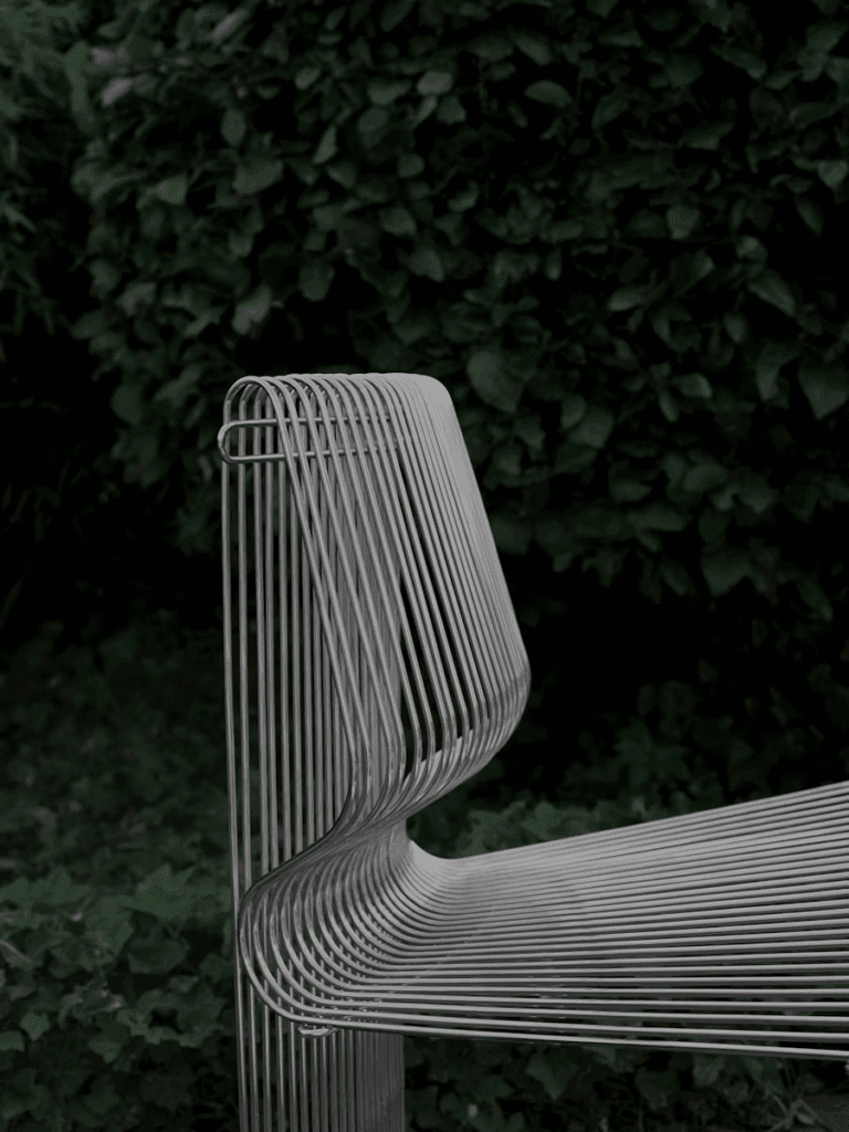 Modern wire bench with an elegant design, surrounded by lush greenery.