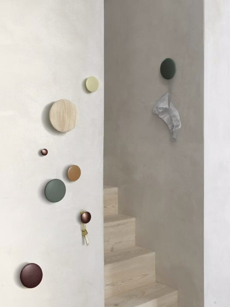A wall featuring various decorative wall hooks in different shapes and colors, alongside a staircase with wooden steps. A piece of white fabric is visible hanging from one of the hooks.