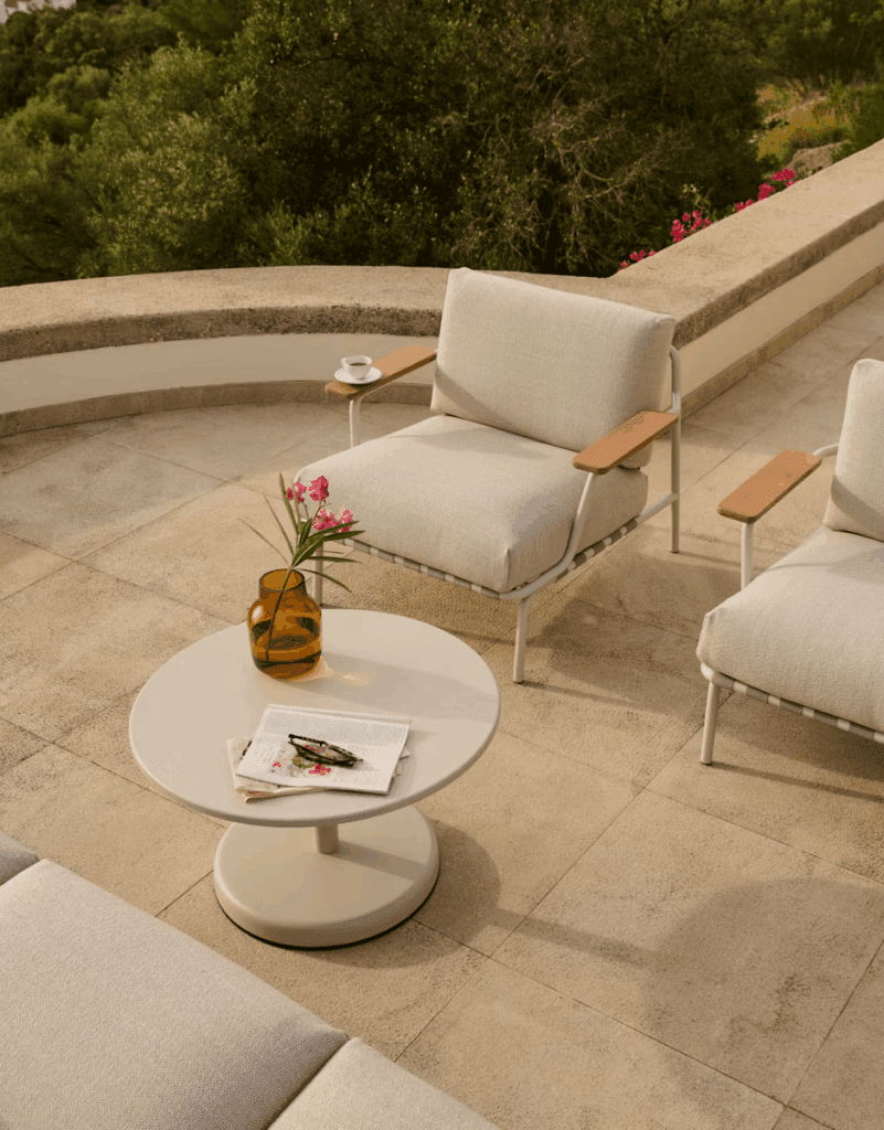 Luxurious outdoor seating area featuring modern armchairs with wooden accents, a round coffee table, a decorative vase with flowers, and a serene natural backdrop.