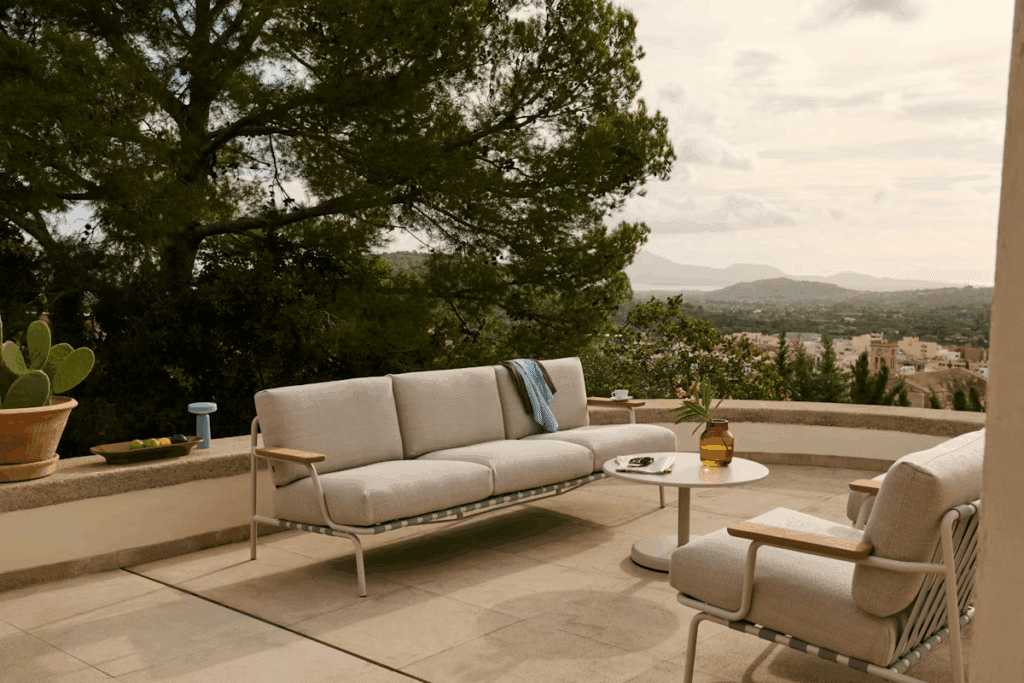 Stylish outdoor seating area featuring a modern sofa and a coffee table, with scenic greenery and distant mountains in the background.