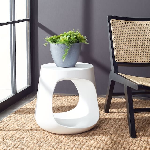 Modern outdoor side table with a potted plant, styled alongside a woven chair, against a dark wall.