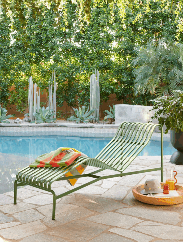 Lounge chair with colorful towels beside a pool, surrounded by lush greenery and tropical plants.