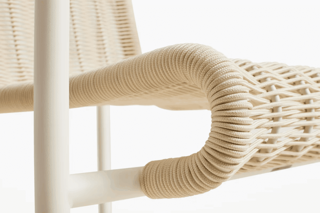 Close-up view of a modern outdoor chair with a woven seat and armrest, showcasing intricate rope detailing and a light color palette.