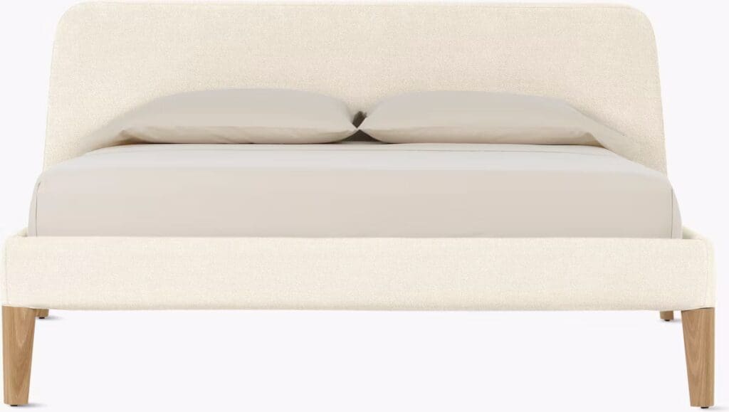 A modern bed with a soft, light-colored upholstered headboard and two flat pillows, set on wooden legs.
