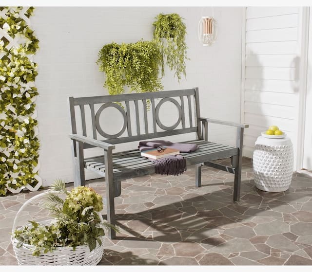 Modern outdoor bench with decorative details, accompanied by potted plants and a stylish white side table, situated on patterned stone flooring.