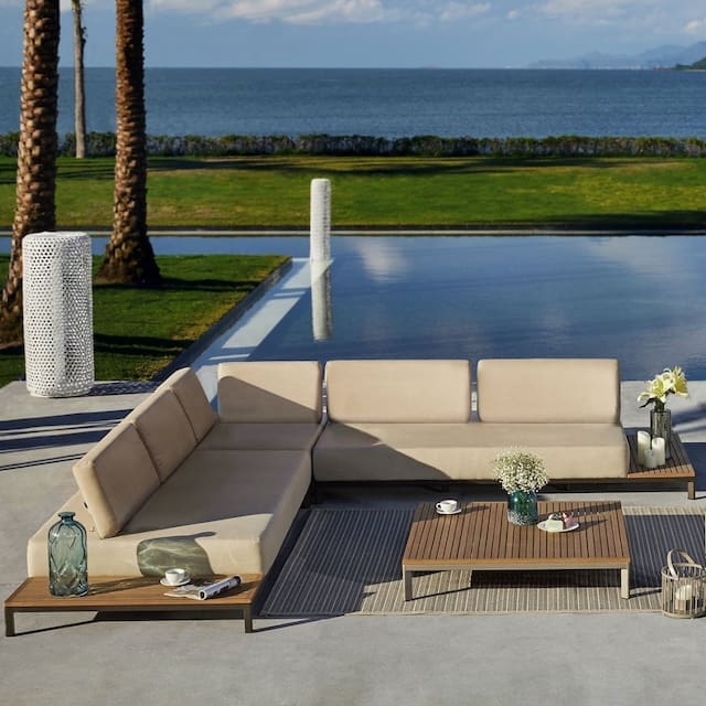 Luxurious outdoor lounge area with a modern sectional sofa, wooden coffee table, and decorative plants, overlooking a serene ocean view.
