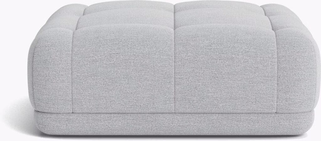 A modern gray ottoman with a tufted design, featuring rounded edges and soft fabric upholstery.