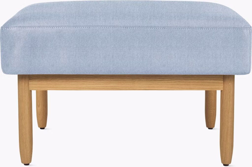 A modern ottoman with a light blue upholstered top and wooden legs, suitable for contemporary living spaces.