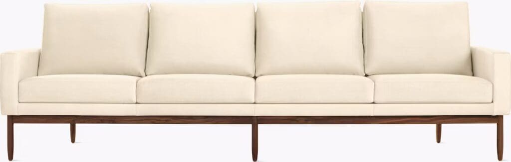 A modern white sofa with a minimalist design featuring plush cushions and wooden legs.