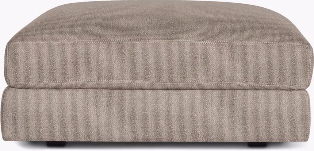A close-up view of a beige upholstered ottoman with a simple, modern design.