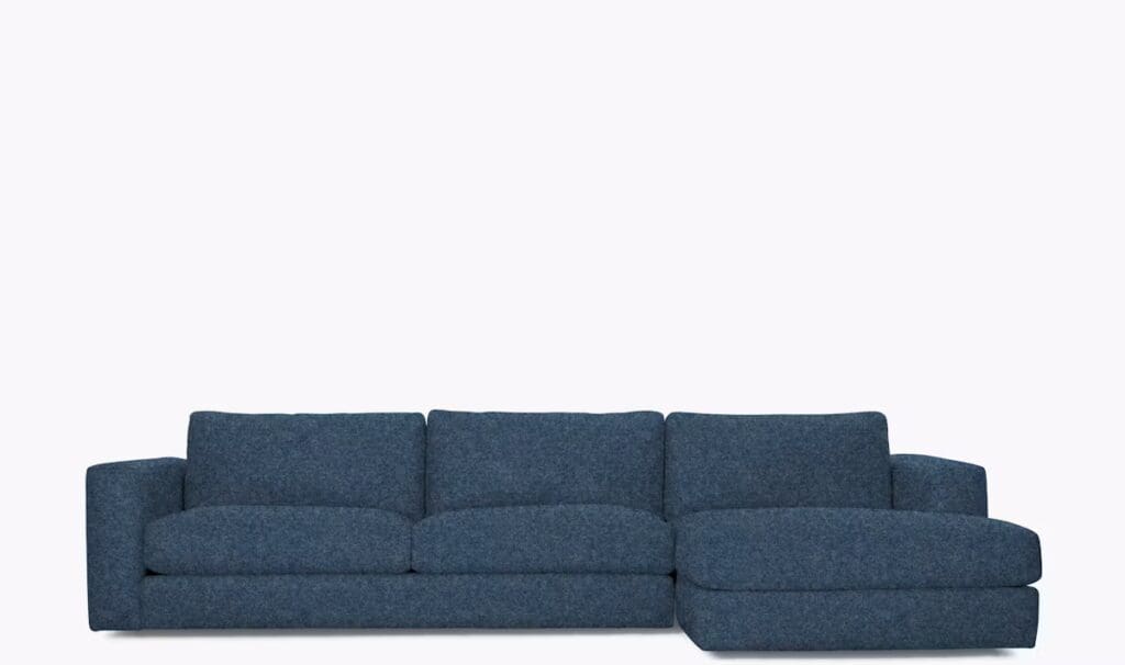 A modern blue sectional sofa with plush cushions and a chaise lounge on one side, set against a neutral background.
