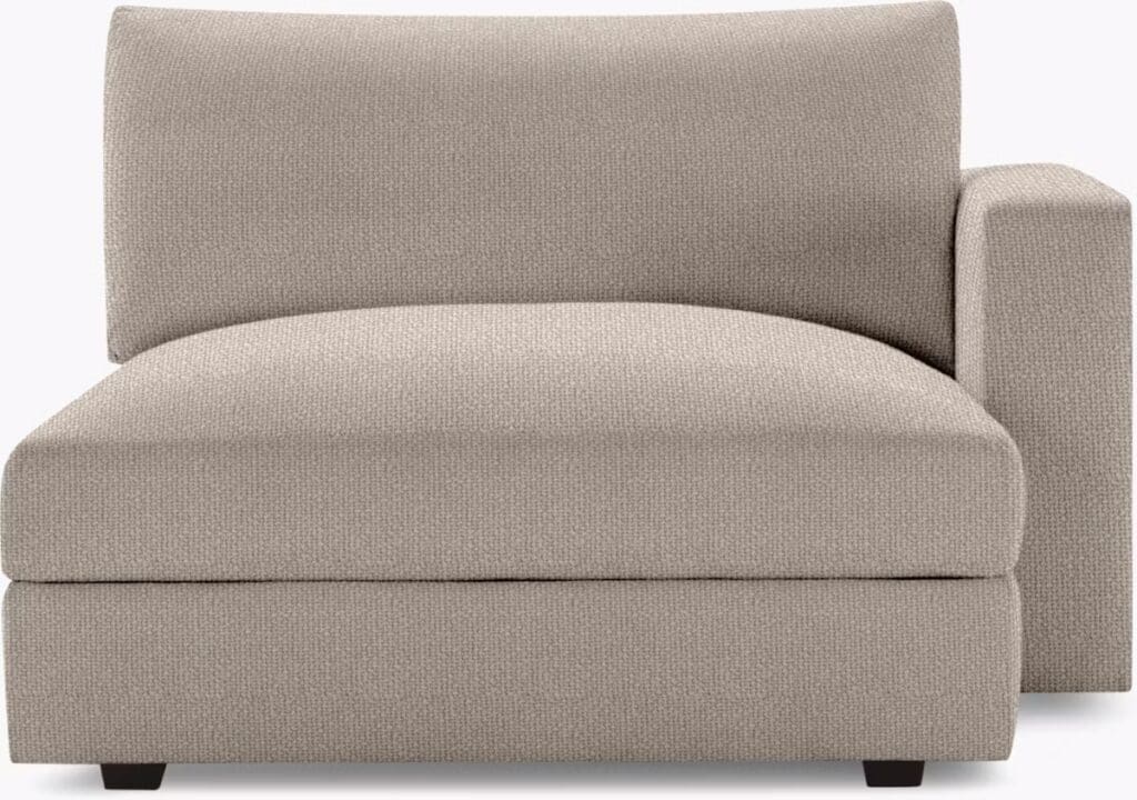 A beige chaise lounge with a low back and an armrest on one side, featuring a textured fabric design.