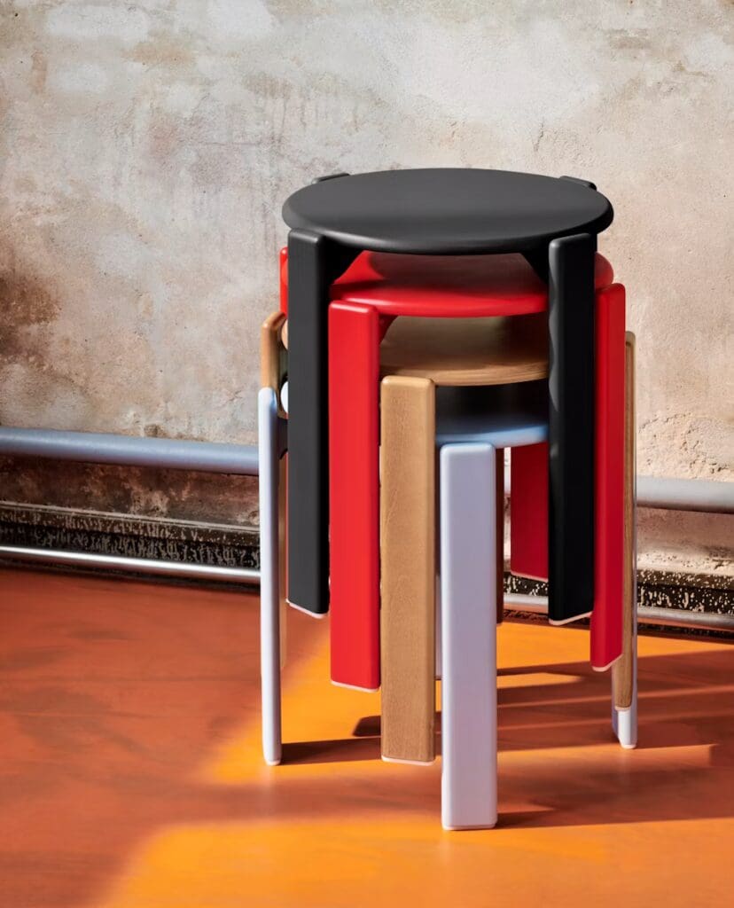 A colorful set of stackable stools with a black top and various colored legs, positioned against a textured wall.