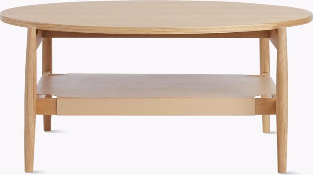 A modern round coffee table made of light wood featuring a flat top and a lower shelf.