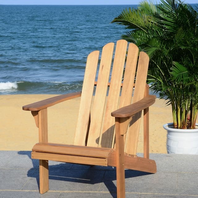 Wooden Adirondack chair facing a sandy beach and ocean, surrounded by greenery.