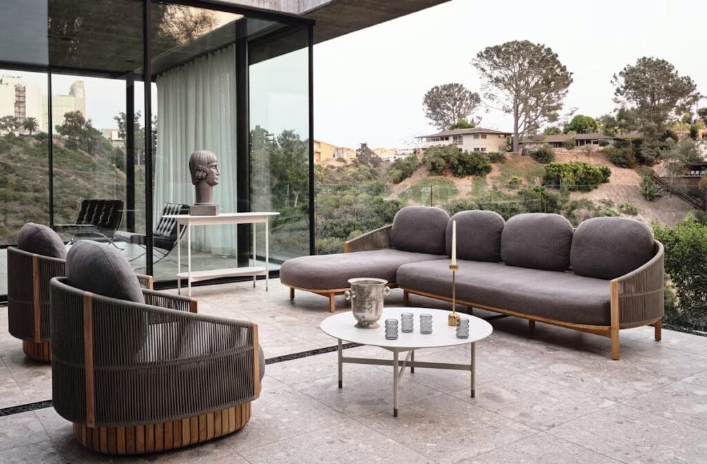 Contemporary outdoor seating area featuring a sectional sofa, armchairs, and a coffee table. The space has a view of lush greenery and hills, with modern design elements highlighted.