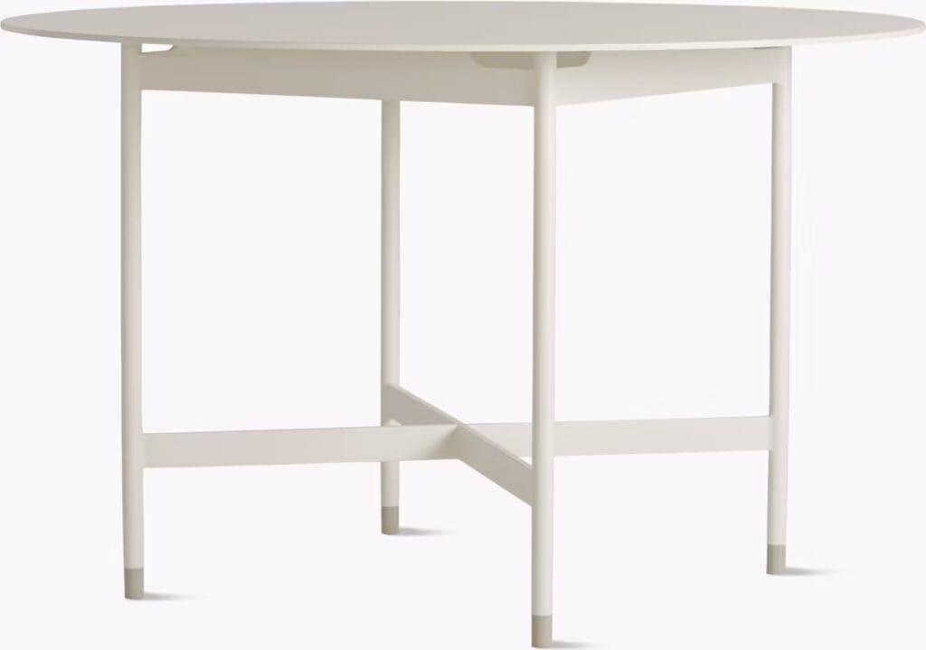 A modern round table featuring a minimalist design with a light-colored top and slender legs.