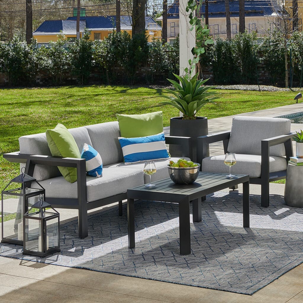 Modern outdoor seating area featuring a gray sofa with colorful cushions, a coffee table, and potted plants, set on a lawn.