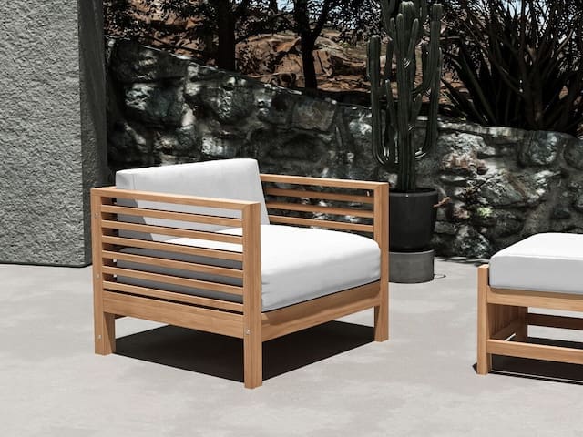 Modern outdoor seating featuring a wooden armchair with white cushions, surrounded by natural stone and greenery.