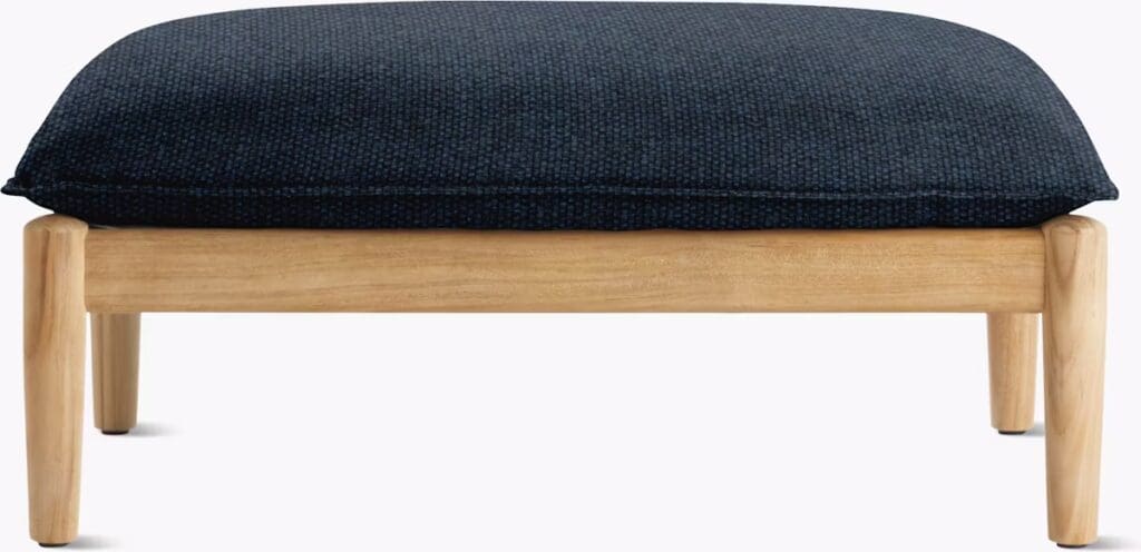 A modern ottoman with a dark blue cushion top and light wood base, showcasing its simple and stylish design.