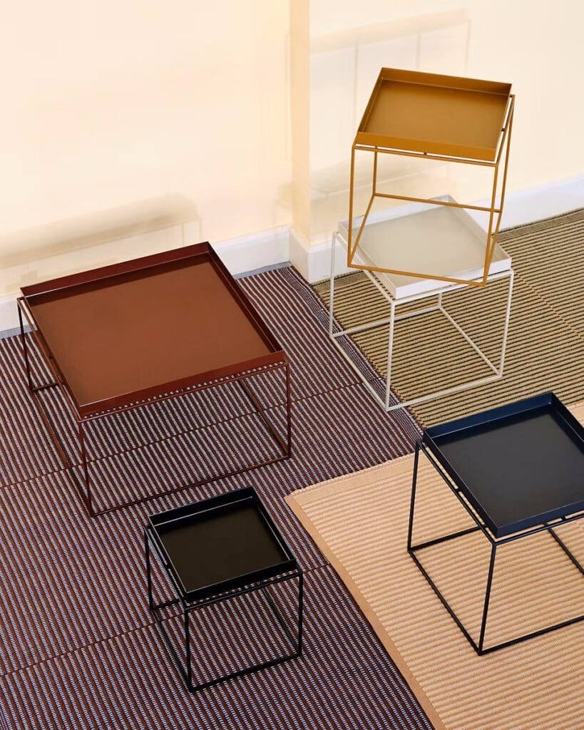 An arrangement of various modern metal side tables in different colors, including brown, gold, black, and white, placed on a striped rug.