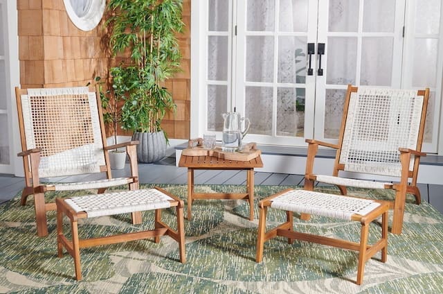 Cozy outdoor seating area featuring two wooden chairs and a small table on a green rug, with a potted plant in the background and large glass doors leading indoors.