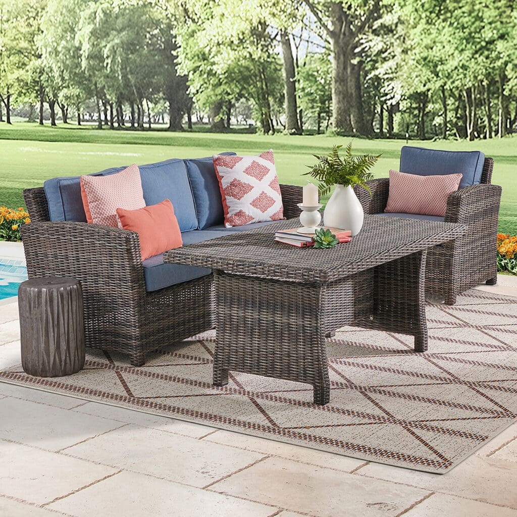Stylish outdoor seating area featuring a wicker sofa with colorful cushions, a coffee table, and a decorative plant, set against a lush green background.