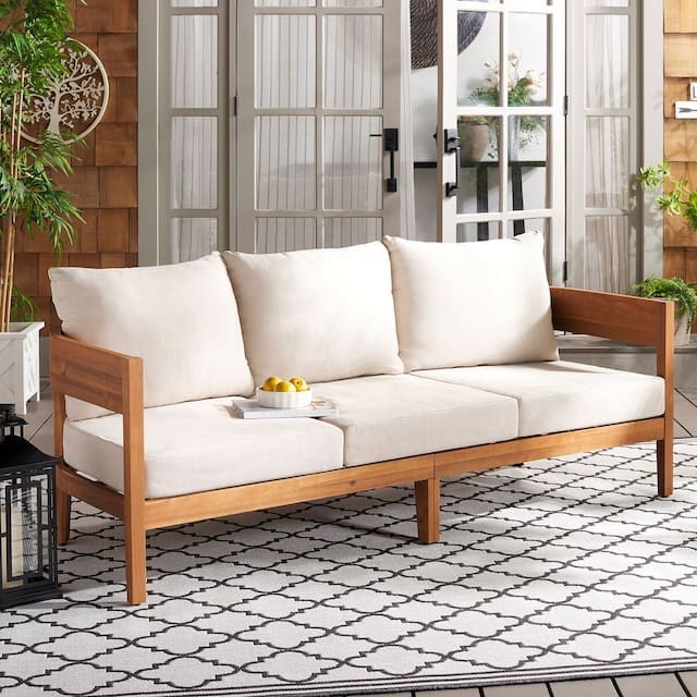 Modern outdoor sofa with beige cushions, set in a stylish patio area featuring wooden sliding doors and decorative plants.