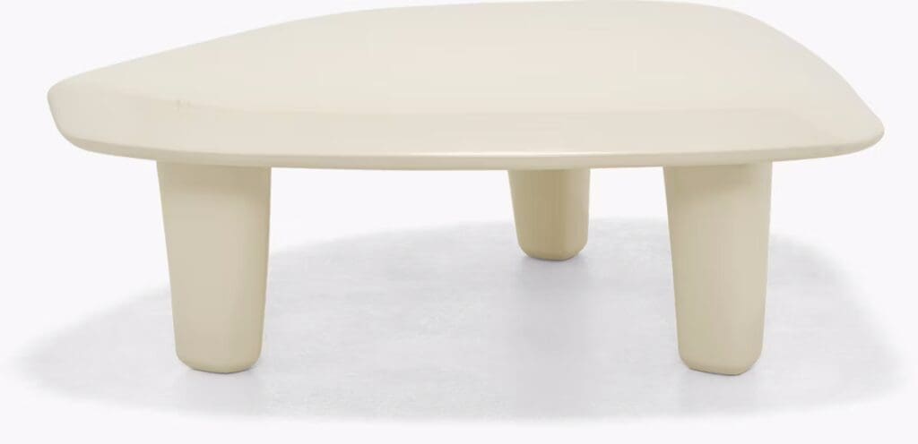 A modern, minimalist coffee table with a smooth, rounded surface and three cylindrical legs, featuring a soft cream color.