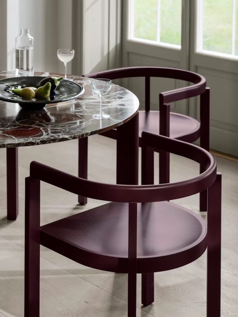 Dining table set featuring a round marble table, deep burgundy chairs, and a bowl of fruit.