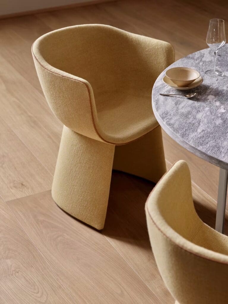 Two modern yellow chairs with a curved design positioned near a round marble table, set on a wooden floor.