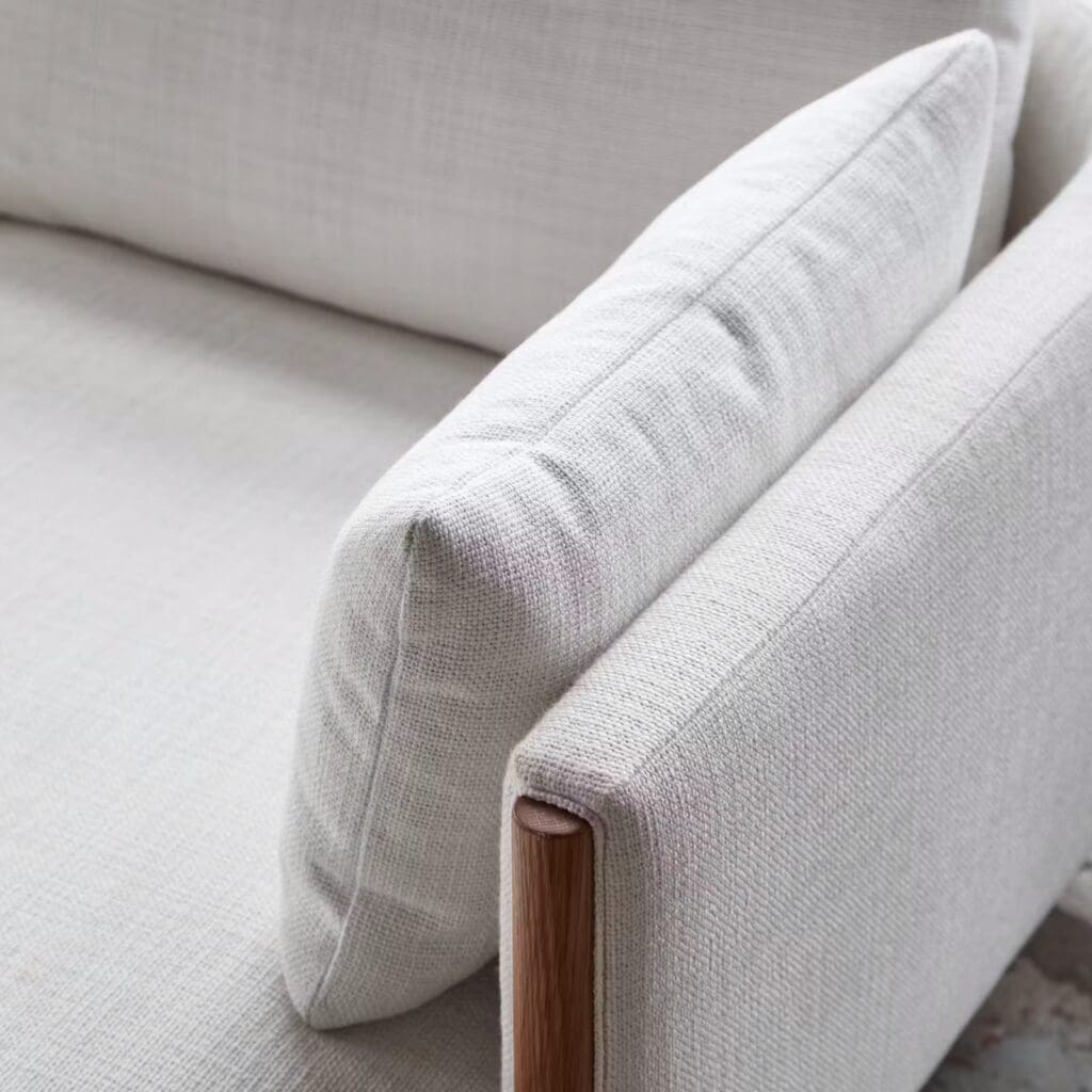 Close-up of a modern sofa featuring a neutral-colored, textured fabric upholstery with a wooden armrest.