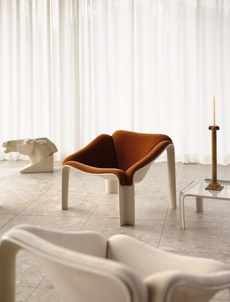 Modern living room featuring a unique brown upholstered chair with a minimalist design, set against a backdrop of sheer white curtains.