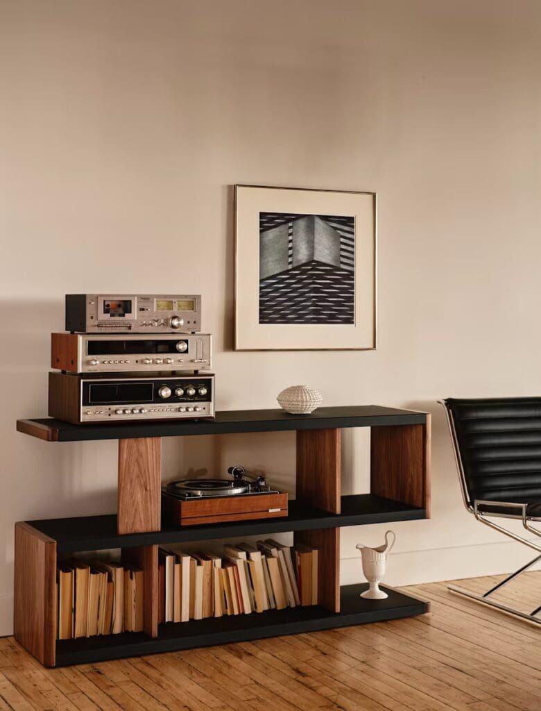 Modern living room with a sleek wooden console table displaying vintage audio equipment, a record player, and books, alongside a black lounge chair and abstract wall art.