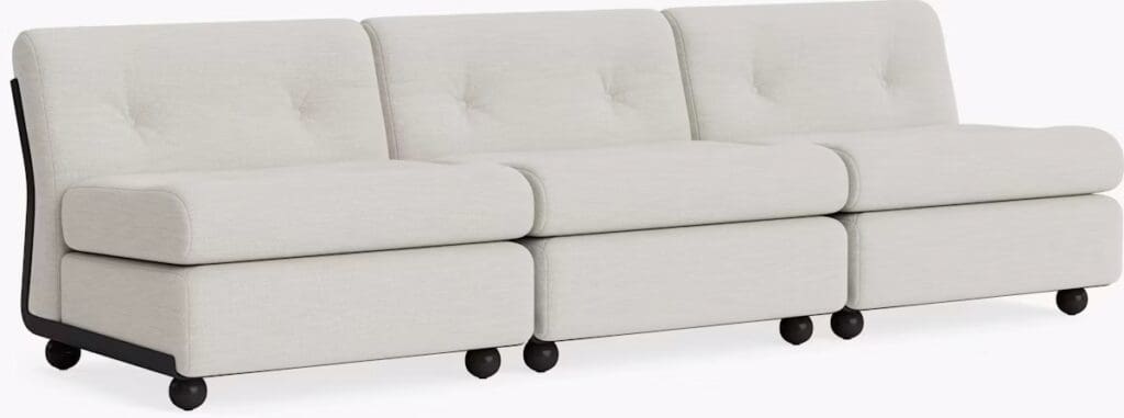 A modern, three-seater sofa with a light fabric upholstery and round black feet, featuring a clean design and button-tufted back cushions.