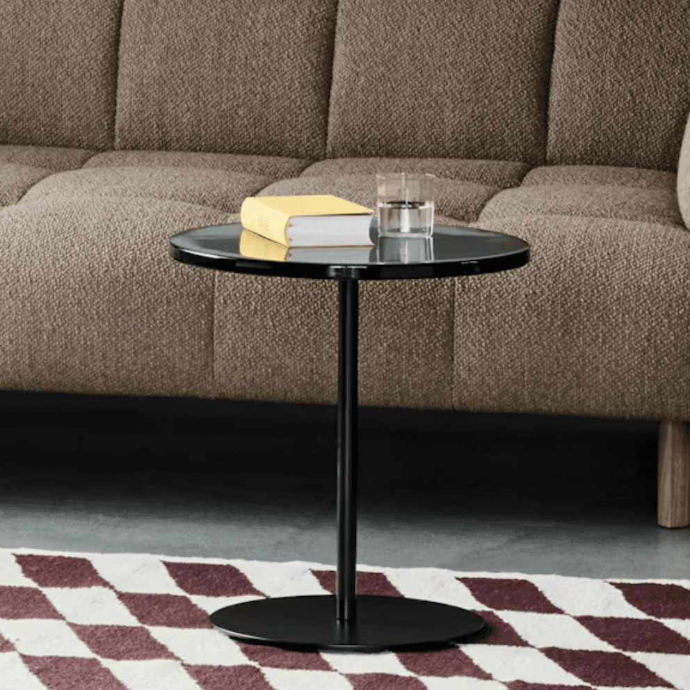 A cozy living room scene featuring a brown textured sofa, a sleek black side table with a glass of water and a yellow book on top, set on a patterned rug.