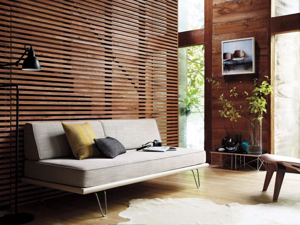 Modern living room featuring a sleek, light-colored sofa with cushions, a wooden slat accent wall, a floor lamp, and a minimalist side table with decorative items.