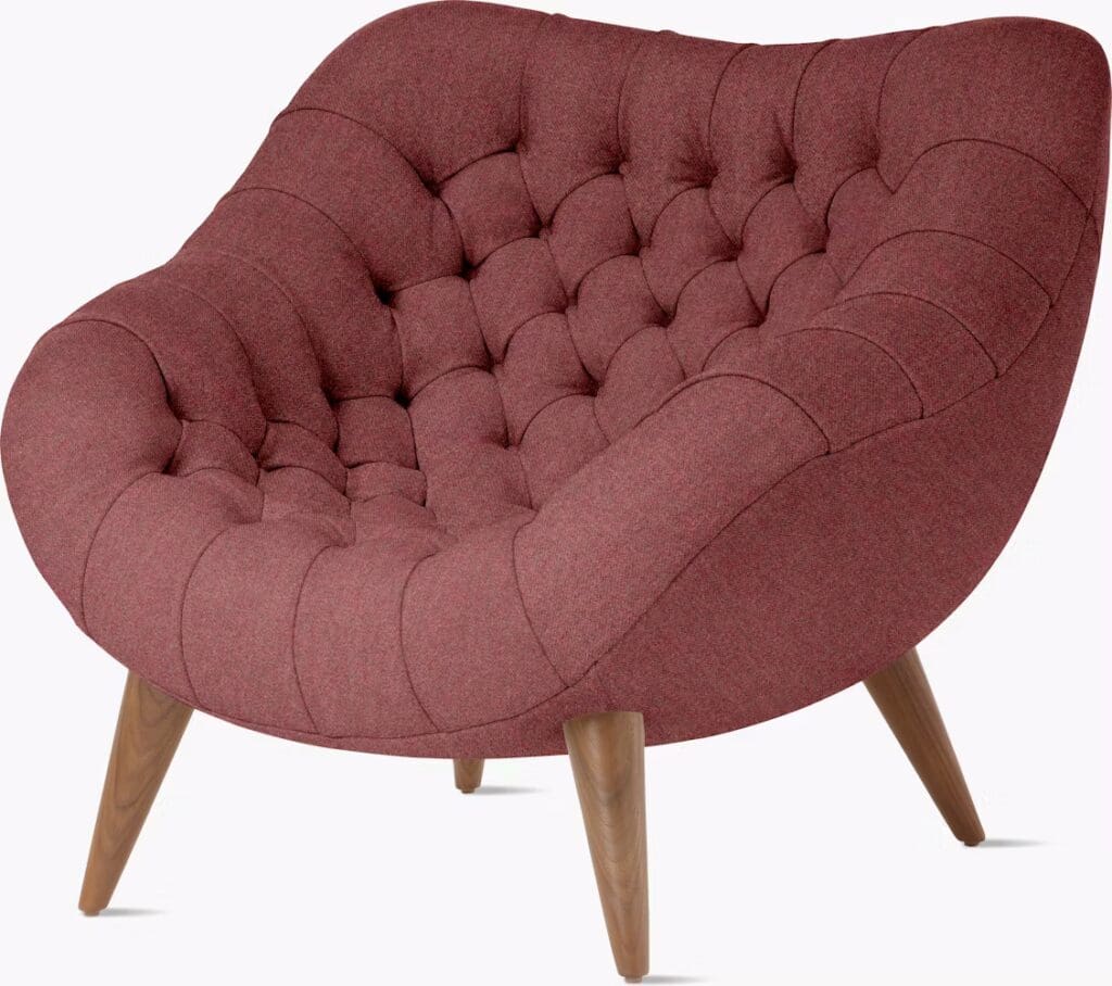 Close-up of a modern burgundy upholstered armchair with tufted detailing and wooden legs.