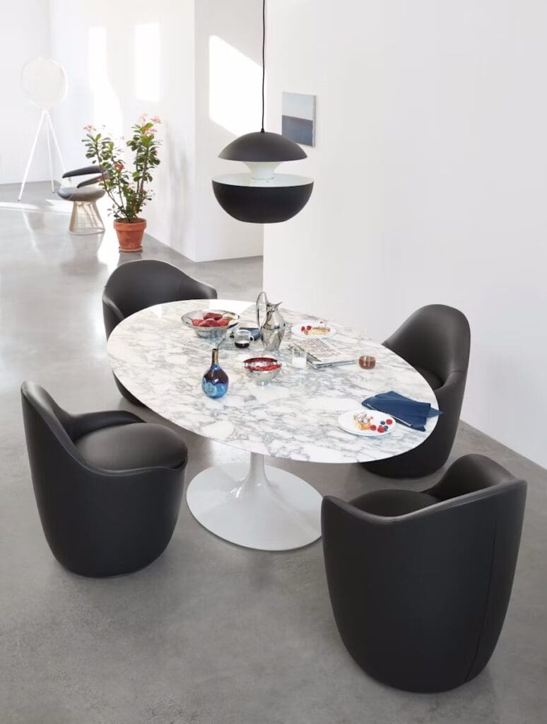 Modern dining area featuring a round marble table surrounded by black leather chairs, with a sleek pendant light above.