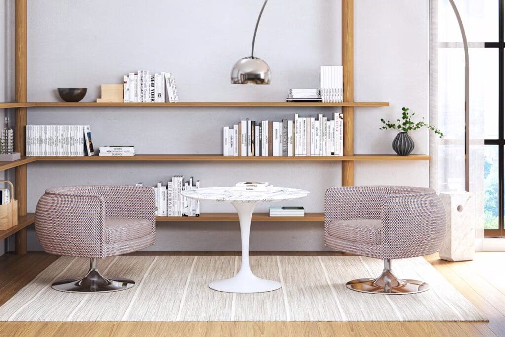 A modern interior featuring two stylish, patterned chairs and a round pedestal table on a light rug, against a backdrop of wooden shelves filled with books.