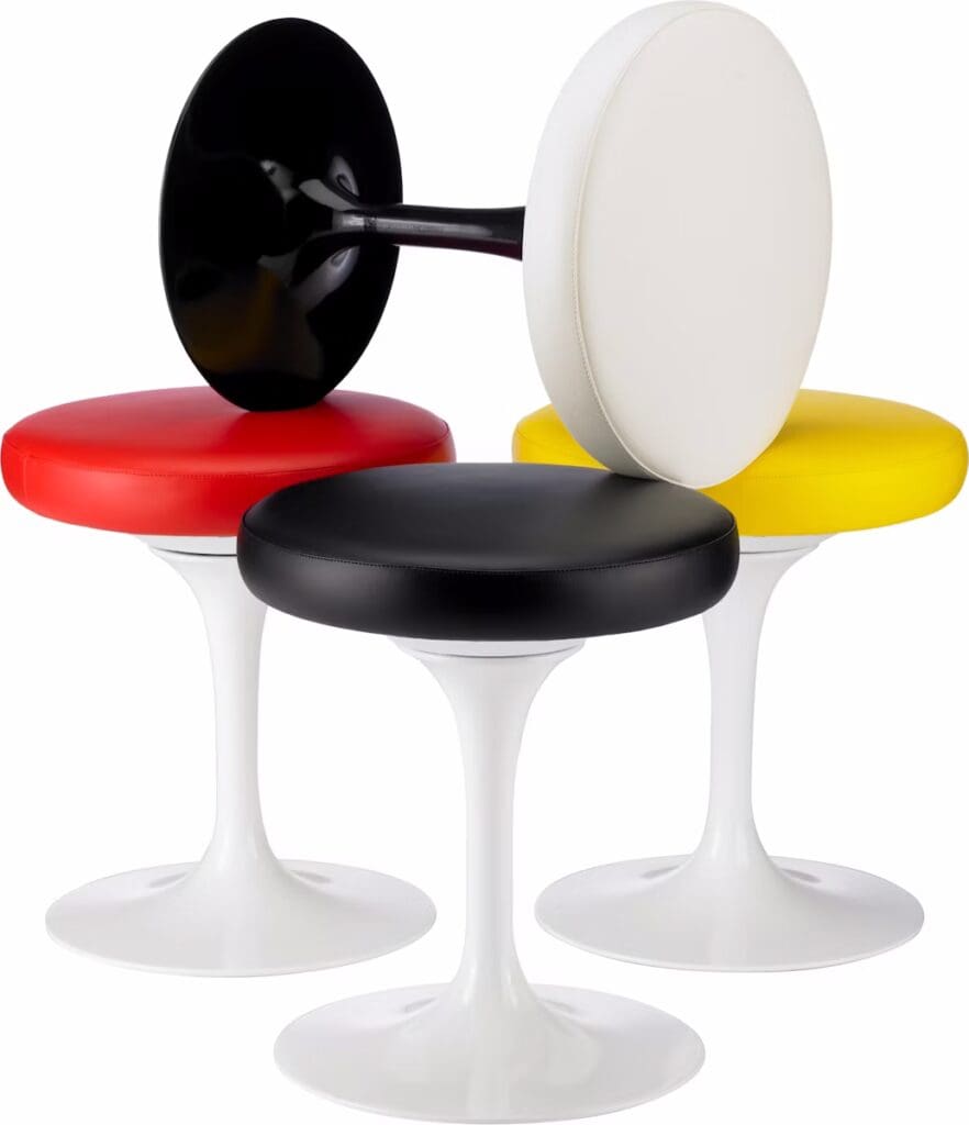 Three colorful stools designed by Eero Saarinen, featuring round seats in red, black, white, and yellow, with white bases resembling tulip shapes.